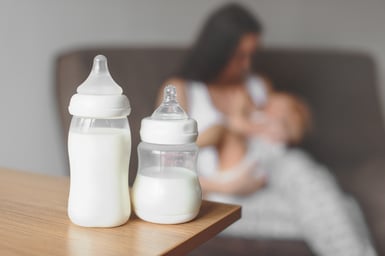 Bottles of breast milk with mom and baby in the background